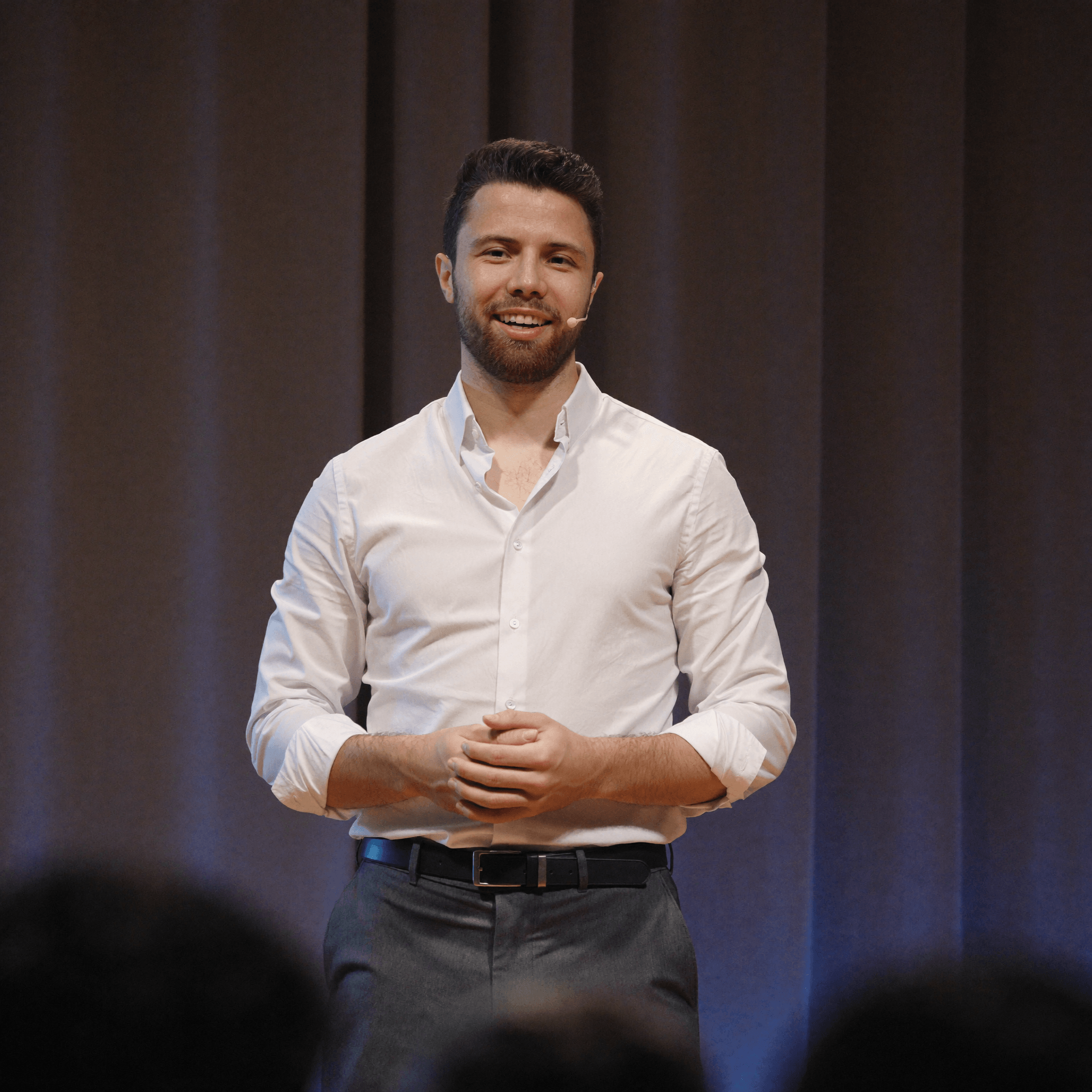 Julius speaking on stage in a white shirt with a headset microphone.